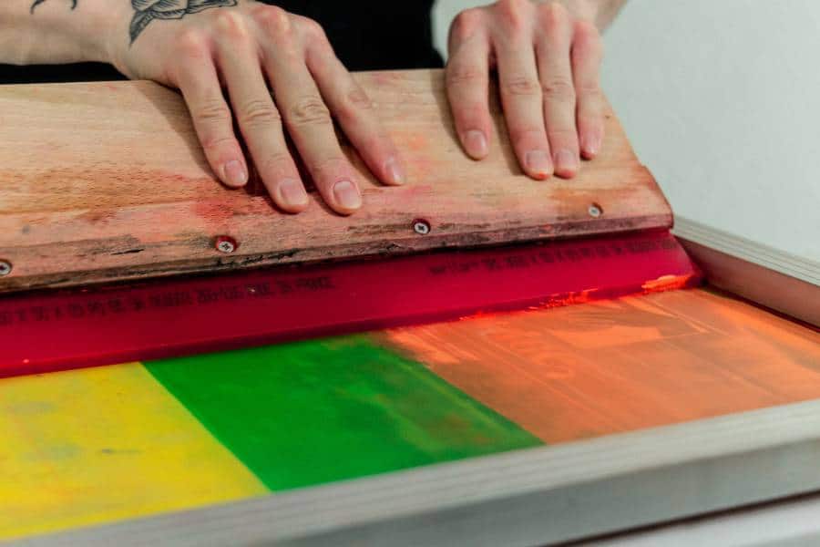 Hands using a squeegee for Austin screen printing on colorful fabric.
